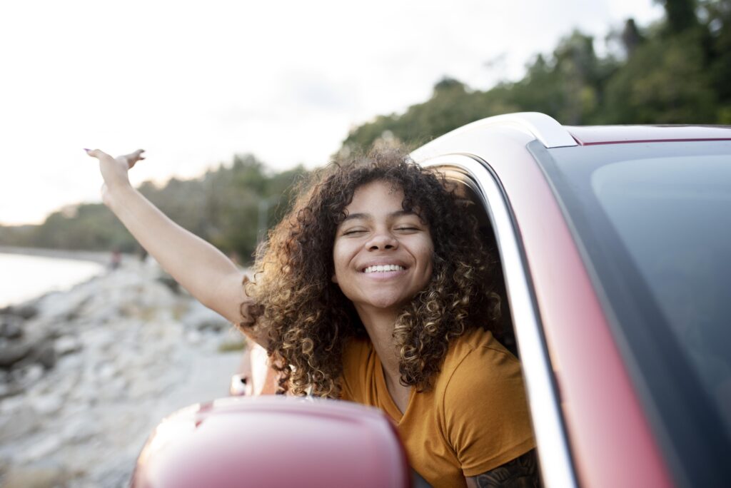 Fille souriante dans une voiture qui tend sa main pour prendre l'air.