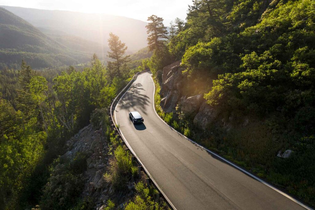 Voiture électrique sur une route de montagne entouré de forêt.